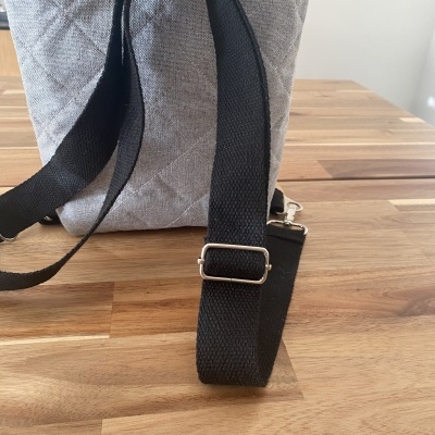 Mochila cinza acolchoada com alças pretas ajustáveis sobre mesa de madeira