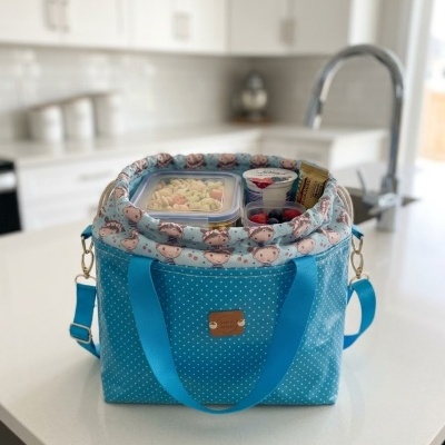 Mala térmica azul com padrão de bolinhas brancas e interior estampado com rostos de ursos numa cozinha moderna branca