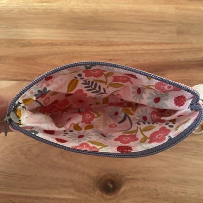 Interior de bolsa pequena com padrão floral colorido e fecho cinzento