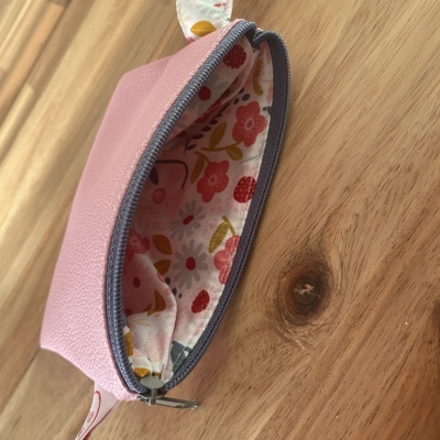 Bolsa pequena rosa com fecho aberto mostrando interior estampado de flores.
