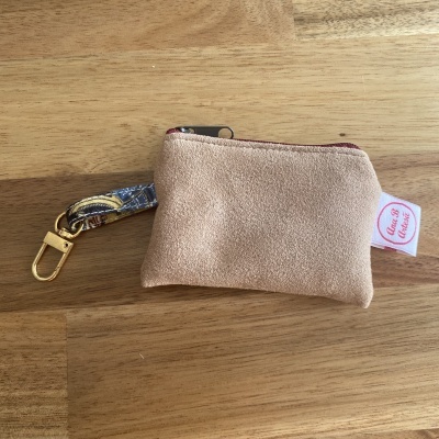 Necessaire ou carteira bege em tecido tipo camurça com fecho bordeaux e pega com padrão colorido.