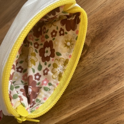 Bolsa pequena branca com fecho amarelo e interior floral colorido sobre madeira