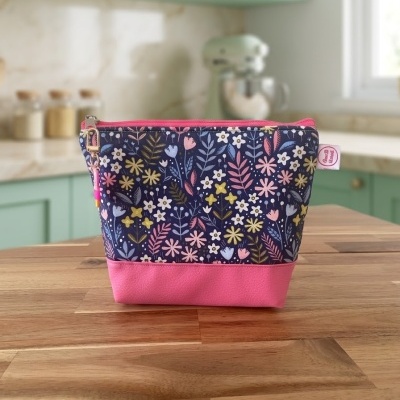 Necessaire floral azul com base cor-de-rosa sobre mesa de madeira numa cozinha.