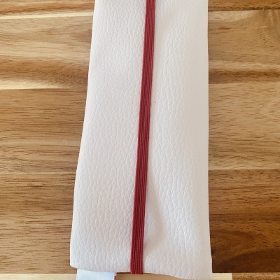 Estojo branco com elástico vermelho sobre madeira