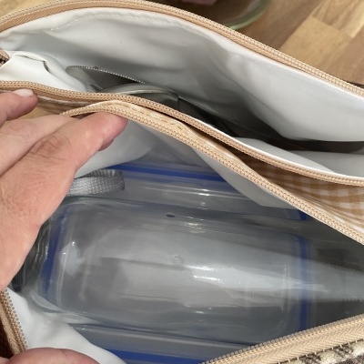 Saco térmico aberto com utensílios e recipientes dentro sobre mesa de madeira.