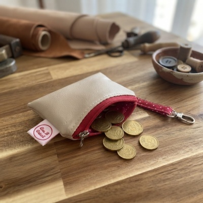 Bolsa pequena de couro branco com fecho vermelho aberta com moedas douradas espalhadas