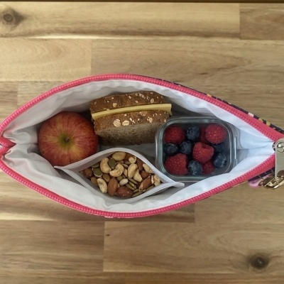 Bolsa térmica aberta com maçã, sanduíche, frutos secos e bagas sobre mesa de madeira.