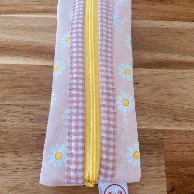 Estojo de tecido rosa com margaridas e fecho amarelo sobre mesa de madeira clara
