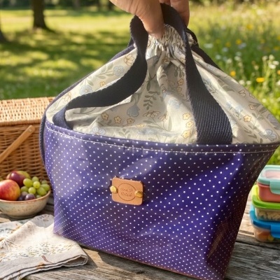 Saco térmico azul com bolinhas brancas e interior floral, ao ar livre numa mesa de madeira