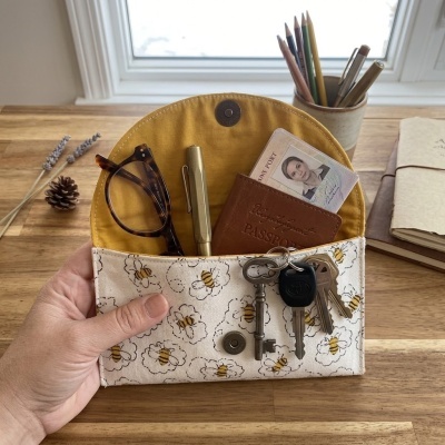 Carteira de tecido estampado com abelhas, contendo óculos, caneta, carteira com passaporte e chaves