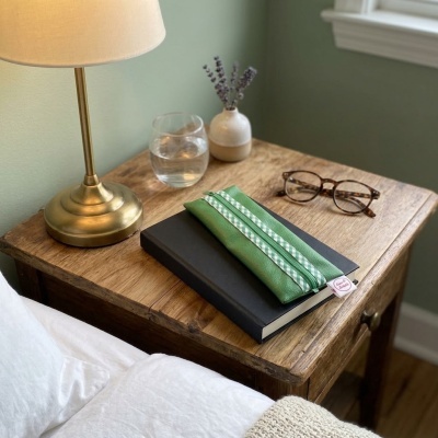 Mesa de madeira com candeeiro, vidro de água, vaso, livro, estojo verde e óculos