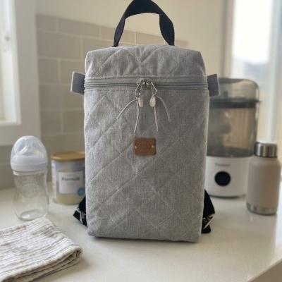 Mochila térmica cinza acolchoada com fecho e alça preta numa bancada de cozinha branca