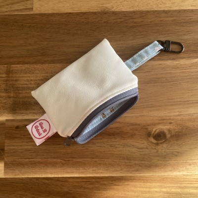 Porte-chaves em tecido branco com fecho azul claro e etiqueta com texto Club House