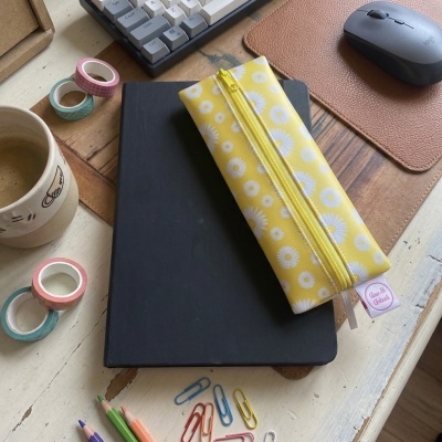 Estojo amarelo com flores brancas e fecho, em ambiente de escritório