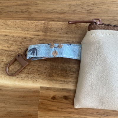 Bolsa bege com fecho castanho e alça azul com padrão de folhas sobre madeira