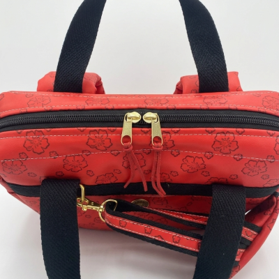 Mochila vermelha com padrão floral, alças pretas e puxadores dourados.