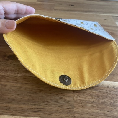 Estojo em tecido amarelo e branco com padrão de abelhas sendo aberto por uma mão
