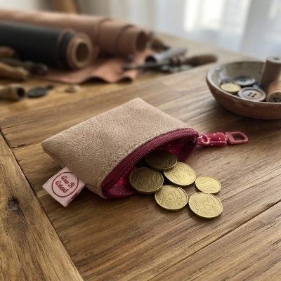 Bolsa pequena bege com fecho rosa e moedas de euro douradas em mesa de madeira