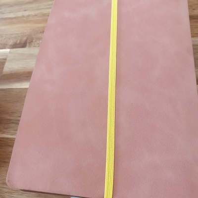 Caderno rosa com elástico amarelo sobre superfície de madeira