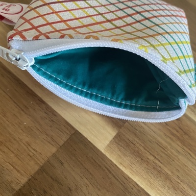 Estojo pequeno colorido com fecho branco aberto exibindo interior verde-azulado