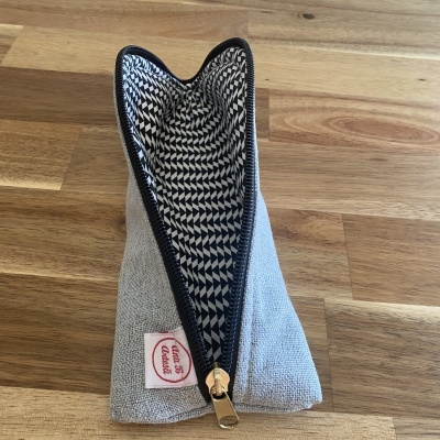 Necessaire cinzenta clara com fecho preto e interior estampado em preto e branco, com etiqueta ULTRA 51 Astoria, em superfície de madeira clara.