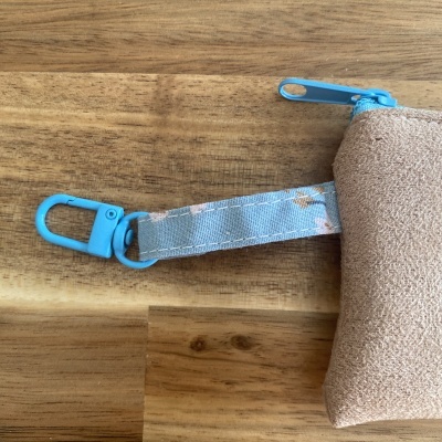 Bolsa ou estojo castanho com zipper azul numa superfície de madeira.