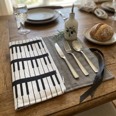Estojo de talheres com padrão de piano aberto na mesa com talheres, pão e frasco decorativo.