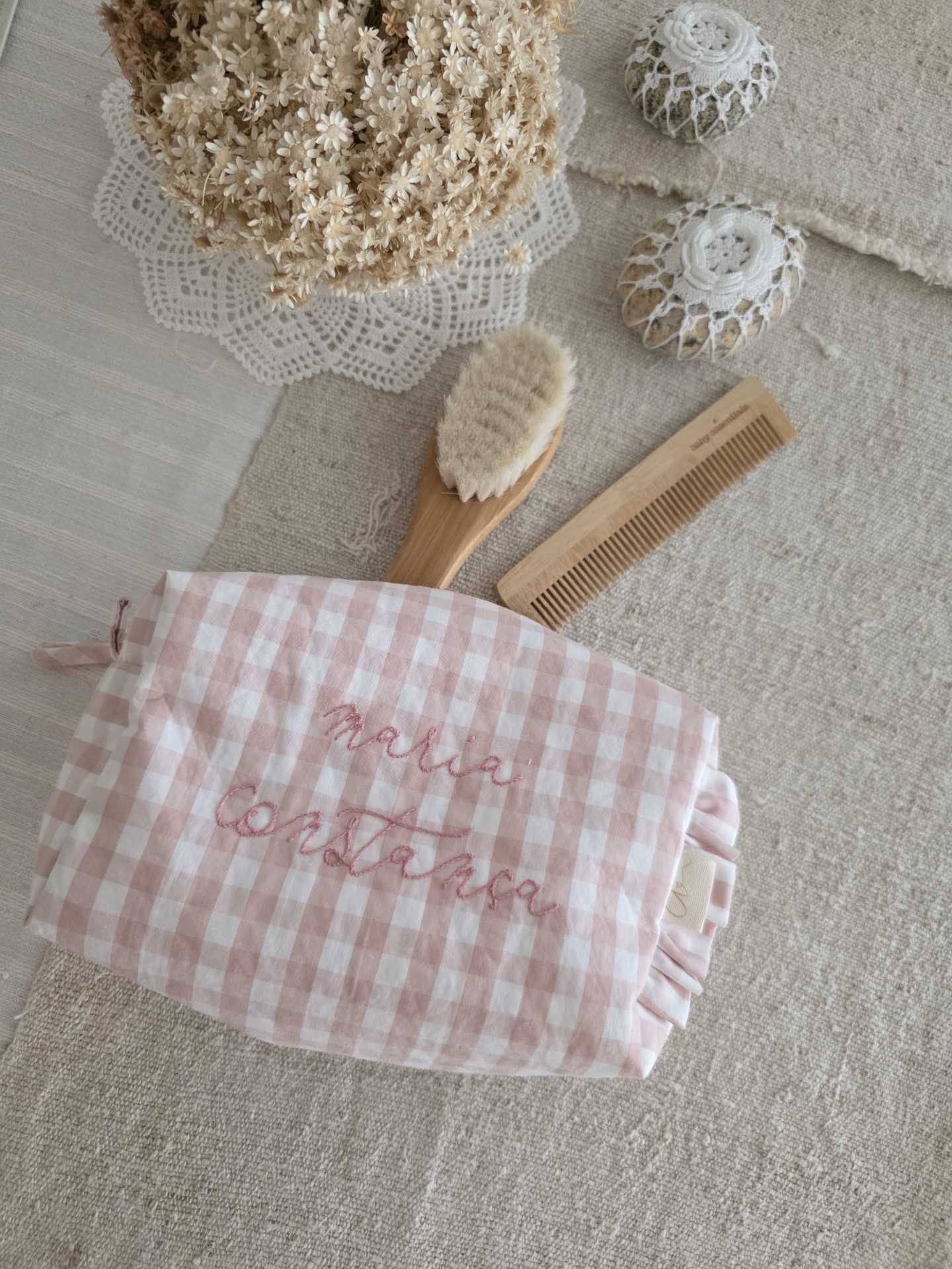 saquinho necessaire Necessaire rosa e branco com nomes bordados, escova e pente de madeira sobre tecido bege e toalha com renda