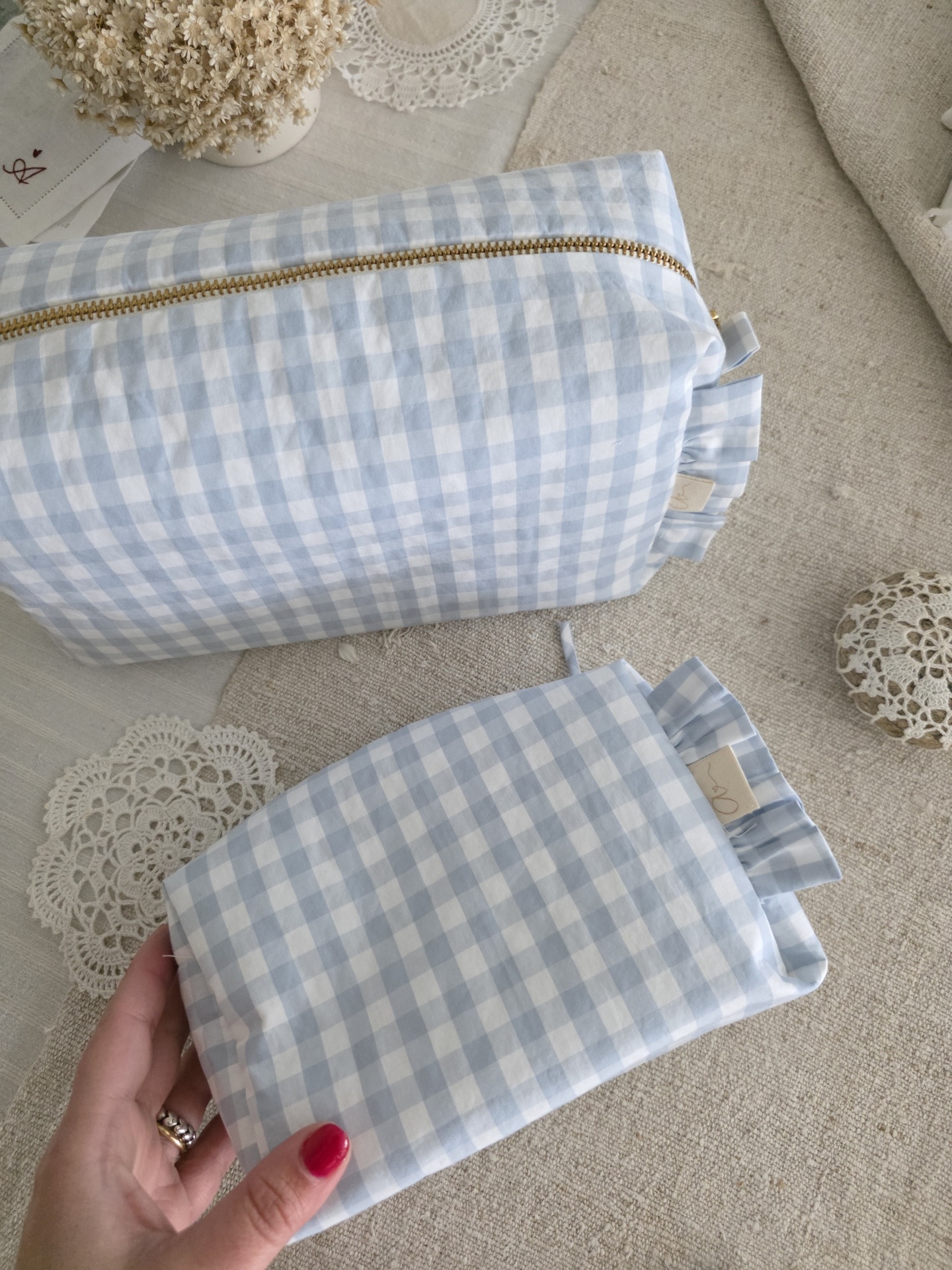 saquinho necessaire Duas bolsas xadrez azul claro e branco com fecho dourado e sem, em superfície bege com rendas brancas