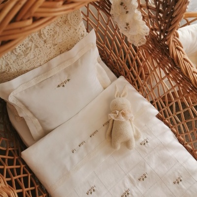 Berço de vime com roupa de cama branca bordada e ursinho de crochê creme