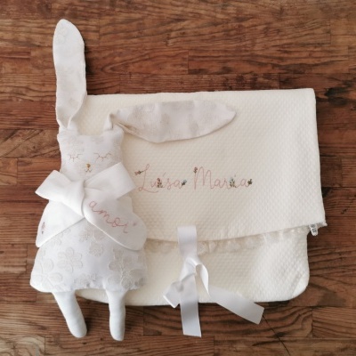 Saco branco bordado com brinquedo de pelúcia em forma de coelho sobre madeira