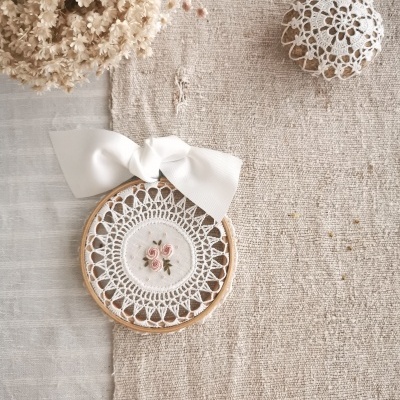 Argola de bordado com flores bordadas e laço branco sobre tecido cru texturizado com flores secas