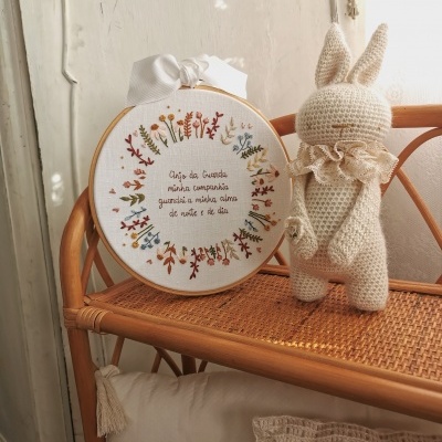 Bordado redondo com flores e texto em aro de madeira e coelho de croché num móvel de vime