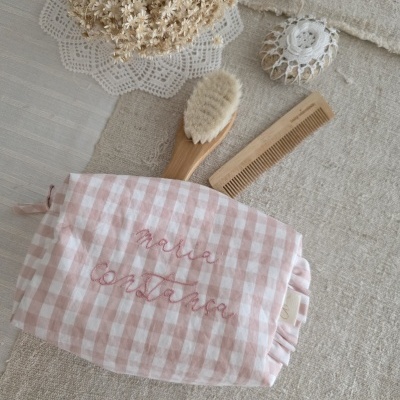 Necessaire rosa e branco com nomes bordados, escova e pente de madeira sobre tecido bege e toalha com renda