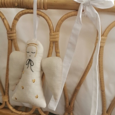 Anjo decorativo branco em tecido pendurado em cama de grades de vime com laço branco