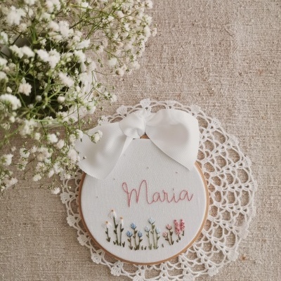 Aro de bordado com o nome Maria e flores, decorado com laço branco, sobre fundo bege e renda