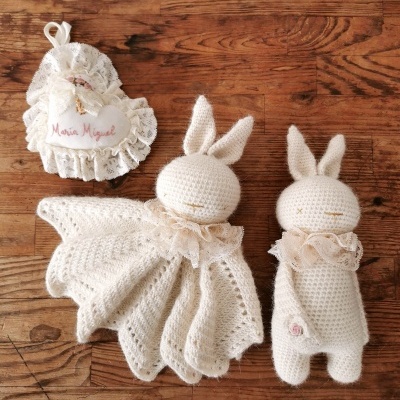 Produtos em croché creme: dois coelhos e um saco decorativo em renda com etiqueta 'Maria Miguel'