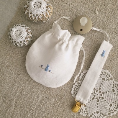 Saco de pano e porta-chupeta brancos com bordado azul e dois pacotes embalados em crochê