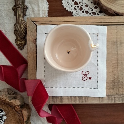 Chávena branca de cerâmica com bordado vermelho e fita vermelha sobre madeira