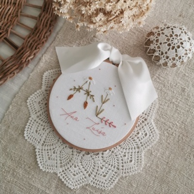 Bordado redondo com flores em tecido branco e laço branco sobre tecido cru.