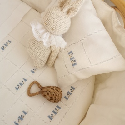 Boneco de crochê branco em forma de coelho com gola rendada sobre almofada branca bordada azul e chocalho de vime