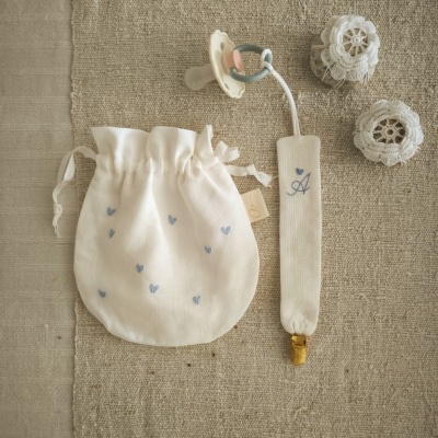 Conjunto de artigos para bebé em tecido cru com detalhes azuis e rendas sobre tecido bege.