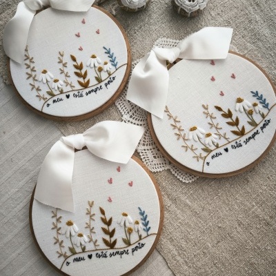 Três bastidores de bordado redondos com decoração floral e texto bordado em tecido branco