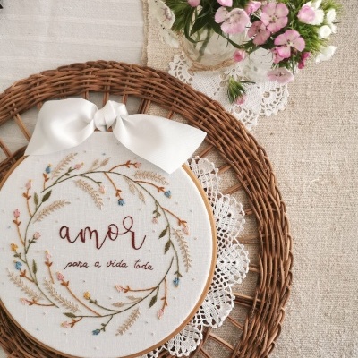 Bastidor bordado com texto amor para a vida toda sobre base de vime e vaso de flores