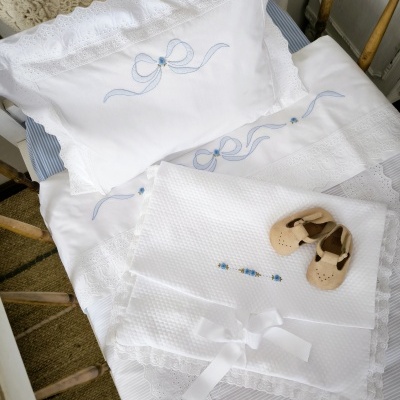 Roupa de cama branca para bebé com bordados azuis e sapatinhos de pele bege.