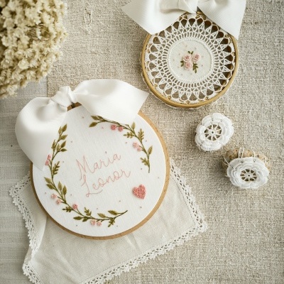Bordados em bastidores de madeira com tecido branco, flores rosa bordadas e fitas brancas