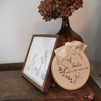 Arranjo decorativo com quadro, bordado e vaso com flores secas num ambiente rústico