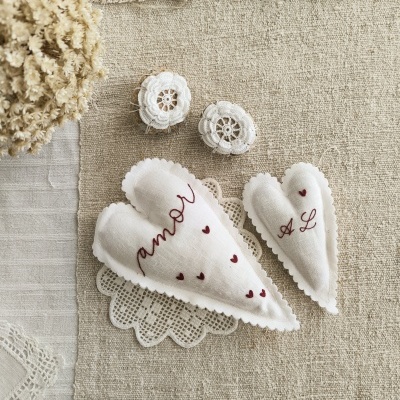 Objetos em tecido branco bordados com texto vermelho e crochê sobre tecido cru