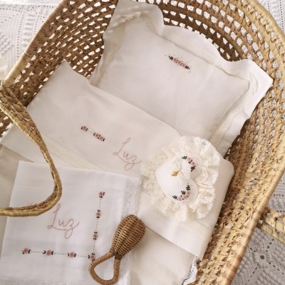 Berço em vime com roupa de cama branca bordada e pente de madeira