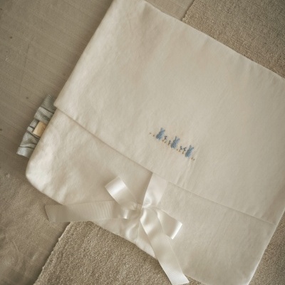 Capa branca de tecido com bordado azul e laço branco